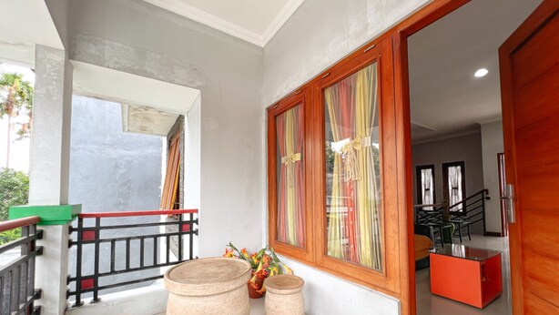 A spacious balcony with a railing, large windows with curtains, and a view of the interior. - Homestay Jogja dekat Ambarukmo by Simply Homy (Depok)