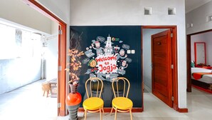 A room with a dark wall decorated with a 'Welcome to Jogja' mural, two yellow chairs, and a tall vase with dried flowers. - Homestay Jogja dekat Ambarukmo by Simply Homy (Depok)