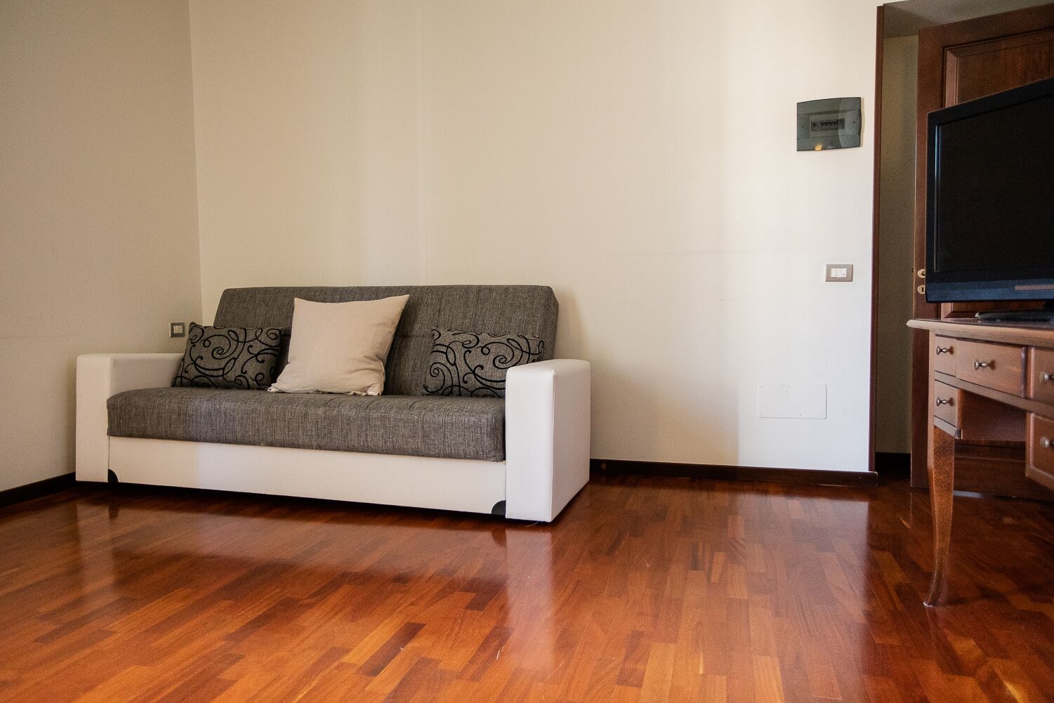 Een woonkamer met een witte bank, decoratieve kussens, een houten kast en een televisie.