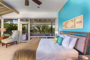 Une chambre avec un grand lit, une chaise, une vue sur l’extérieur et un ventilateur de plafond.