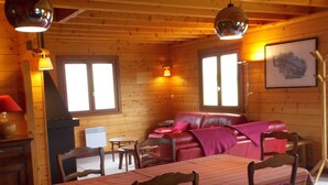 Interior acogedor de una cabaña de madera con una mesa de comedor, sillas, un sofá y una chimenea.