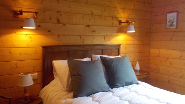 Una habitación con paneles de madera, una cama, dos lámparas de noche y una mesita con lámpara.