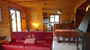 Interior acogedor de una cabaña con un sofá de cuero rojo, una mesa de comedor de madera y una chimenea.