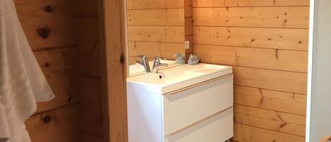 Un baño de cabaña de madera con un tocador blanco, un espejo y un lavabo.
