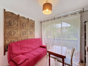 A room with a red sofa, a wooden partition with intricate designs, a table with chairs, and a view through a large window with curtains.