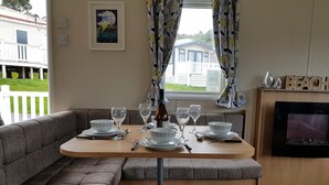 A dining area with a wooden table set for four, a sofa, and a fireplace. - Pool-garden-2br-parking-wifi-sleeps6 (Paignton)