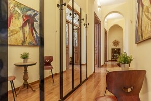 A hallway with wooden flooring, a round table with a potted plant, a modern chair, and a large abstract painting on the wall.