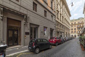Une rue étroite pavée, bordée de voitures garées et de bâtiments historiques à l’architecture classique.