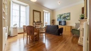A spacious living room with a dining area, a fireplace, and a television. - GuestHost - Elegant 110 sqm apartment, which can accommodate up to 3 people, located on the fourth floor of a period building with lift (not suitable for the disabled). The property, in the Traffic Restricted Area (ZTL), is located in the heart of the hi (Roma)
