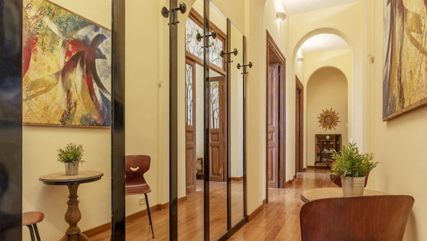 A hallway with wooden flooring, a round table with a potted plant, a modern chair, and a large abstract painting on the wall. - GuestHost - Elegant 110 sqm apartment, which can accommodate up to 3 people, located on the fourth floor of a period building with lift (not suitable for the disabled). The property, in the Traffic Restricted Area (ZTL), is located in the heart of the hi (Roma)