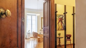 An interior view of a hotel room with a wooden door, a dining area with a table and chairs, and a painting on the wall. - GuestHost - Elegant 110 sqm apartment, which can accommodate up to 3 people, located on the fourth floor of a period building with lift (not suitable for the disabled). The property, in the Traffic Restricted Area (ZTL), is located in the heart of the hi (Roma)
