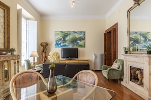Una sala de estar con sofá, sillones, televisor, obras de arte, chimenea y espejo.