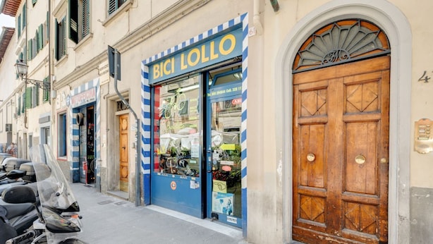 Un escaparate con un toldo azul y blanco a rayas, una puerta de madera y una moto estacionada afuera.