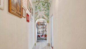 Un pasillo estrecho con suelo de madera, una estantería con diversos objetos y cuadros en las paredes.