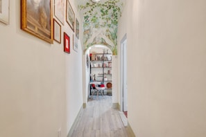 A narrow hallway with a wooden floor, a bookshelf with various items, and framed pictures on the walls.
