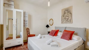 Un dormitorio con cama, armario, silla, un cuadro y una lámpara.