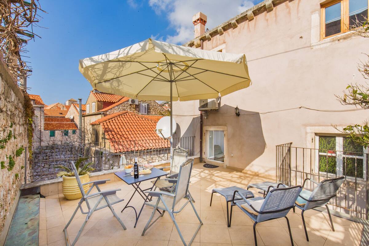 A patio with outdoor furniture, a large umbrella, and a view of neighboring buildings.