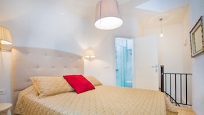 Ein Schlafzimmer mit einem großen Bett, einem roten Kissen, einem Kopfteil, einer Nachttischlampe und einer Tür zu einem Badezimmer.