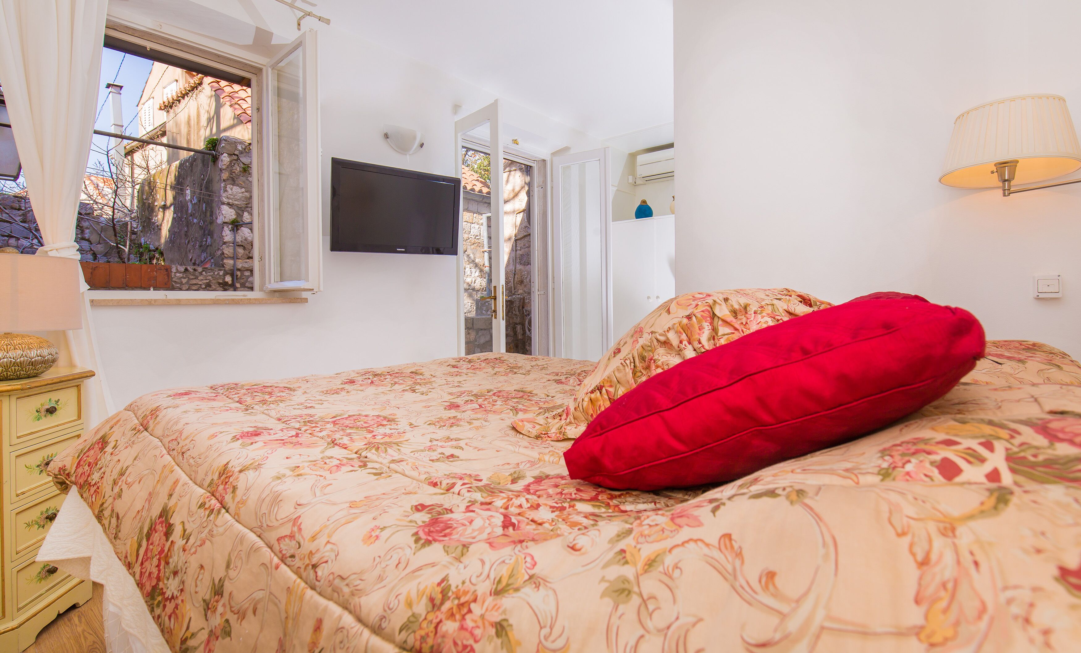 Un dormitorio con cama, televisor, ventana y lámpara.