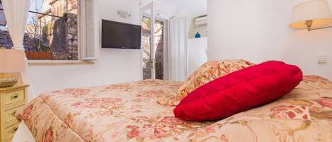Un dormitorio con cama, televisor, ventana y lámpara.