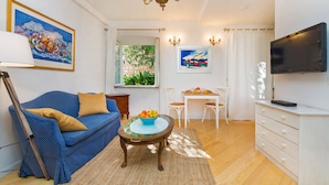 Ein Wohnzimmer mit einem blauen Sofa, einem Couchtisch mit Früchten, einem Fernseher und Kunstwerken an den Wänden.