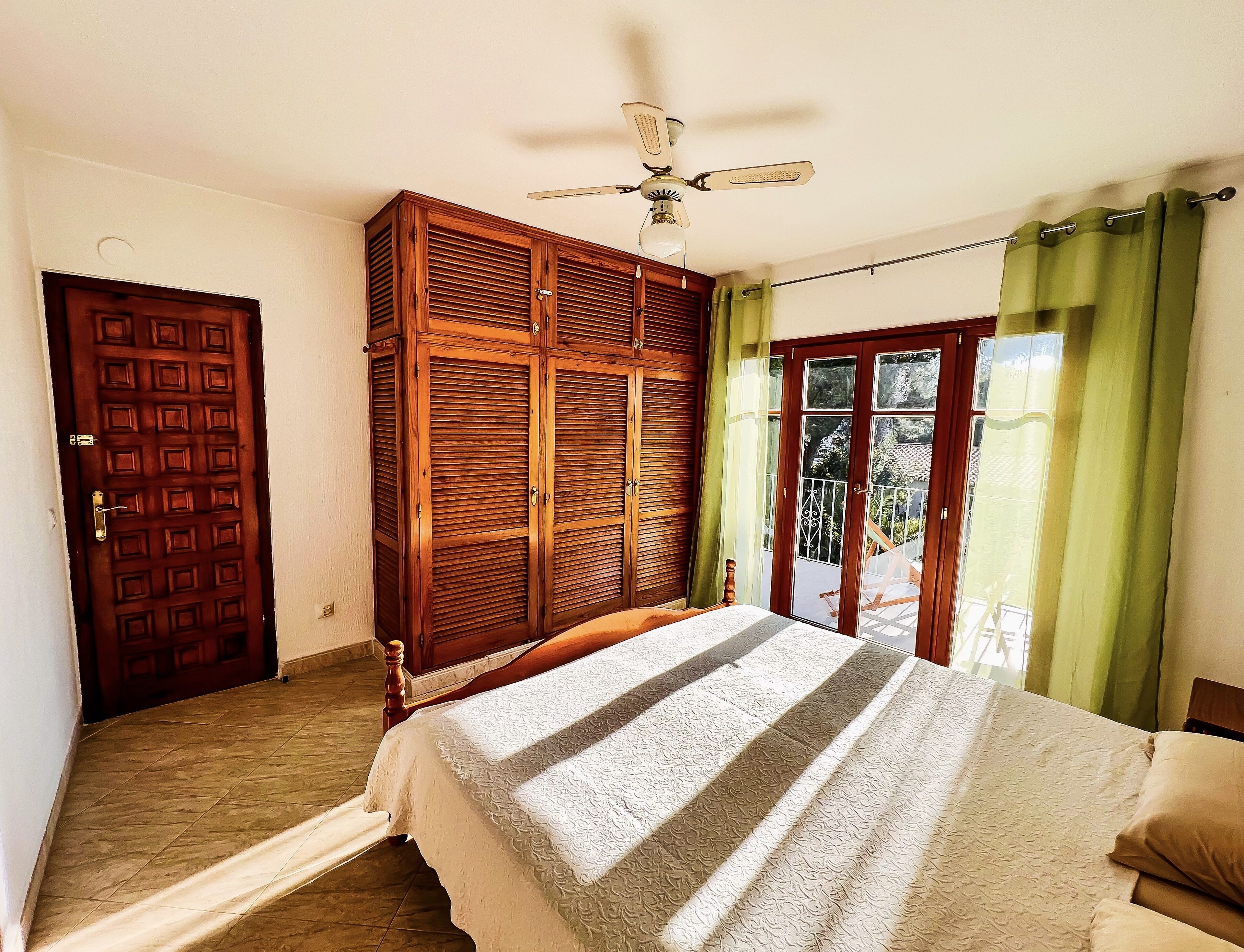 A bedroom with a bed, a wardrobe, a ceiling fan, and a sliding glass door.