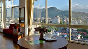 Habitación de hotel con un ventanal grande que ofrece vistas a una ciudad y montañas.