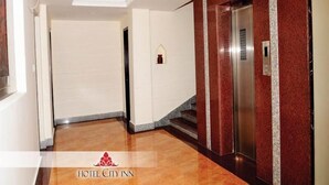 Un pasillo de hotel con suelo de mármol, un ascensor y una puerta con detalles en mármol rojo y blanco.