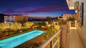 A swimming pool with a stone deck, surrounded by well-lit vegetation and a balcony with a railing. - Poseidonia Syros Cozy House (Poseidonia)