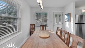 A dining area with a wooden table and chairs, a hanging light fixture, and a view of the outdoors through large windows. - Surf's Up -  Private Heated Pool and Hot Tub - Walk to Beach (St. Augustine)