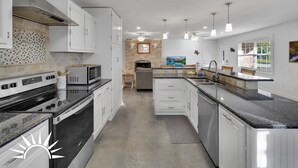 A modern kitchen with white cabinets, a stainless steel range hood, a microwave, and a dishwasher. There are pendant lights and a window with blinds. - Surf's Up -  Private Heated Pool and Hot Tub - Walk to Beach (St. Augustine)