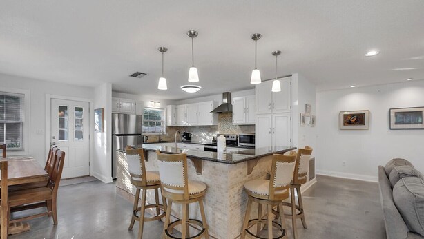 A modern kitchen with a central island, bar stools, stainless steel appliances, and pendant lighting. - Surf's Up -  Private Heated Pool and Hot Tub - Walk to Beach (St. Augustine)
