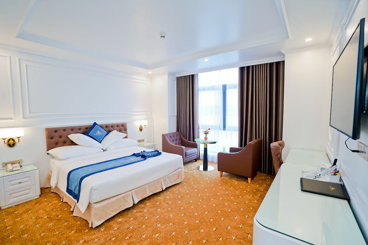 A hotel room with a bed, two armchairs, a desk, a television, and a window with curtains.