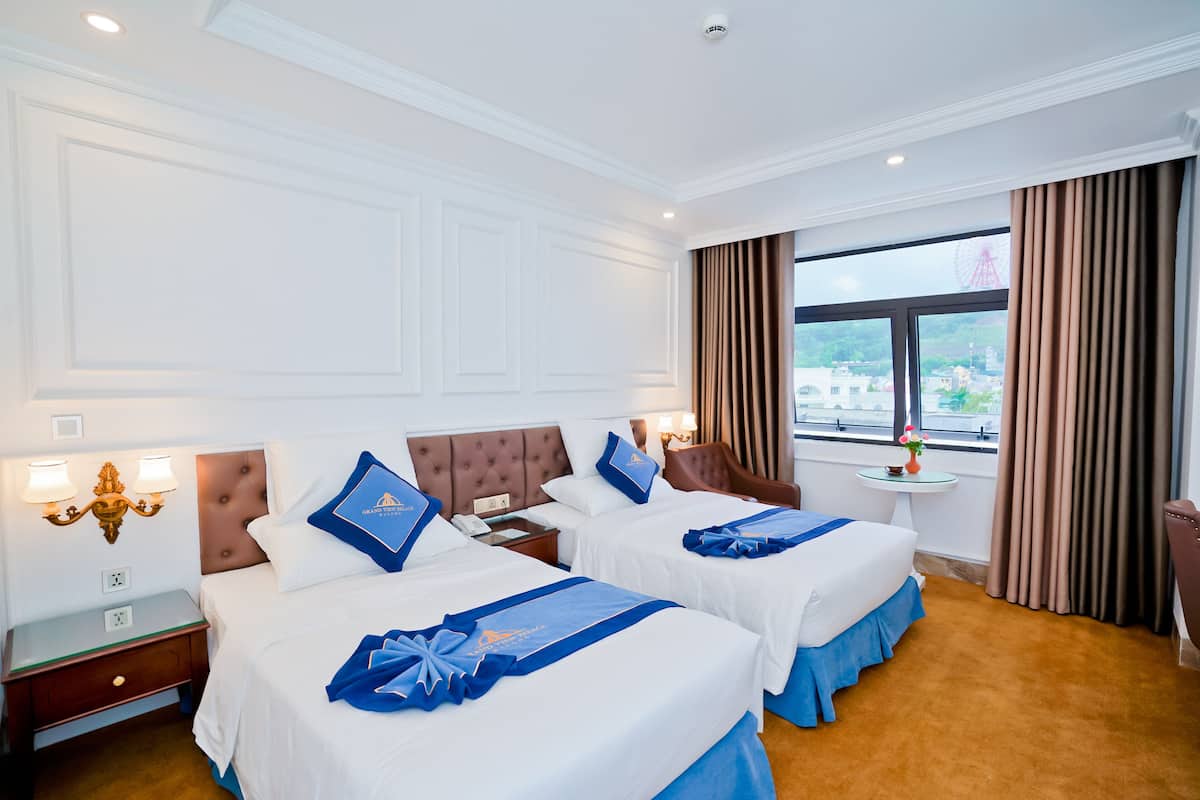 A hotel room with two beds, a small table, and a view of the city.