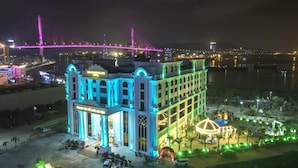 A hotel with a prominent entrance and a well-lit facade, situated near a body of water with a bridge in the background. - Grand View Palace Ha Long Hotel (Hong Gai)