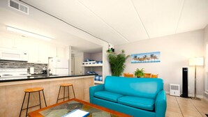 A compact living space with a kitchenette, a blue sofa, a glass coffee table, and a small dining area. - Rayo del Sol II - 201 - WiFi, Walk to the beach (South Padre Island)