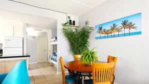 A modern kitchen with white cabinets, a black countertop, and a built-in refrigerator. There is a dining area with a wooden table and chairs, a potted plant, and a painting of palm trees on the wall. - Rayo del Sol II - 201 - WiFi, Walk to the beach (South Padre Island)