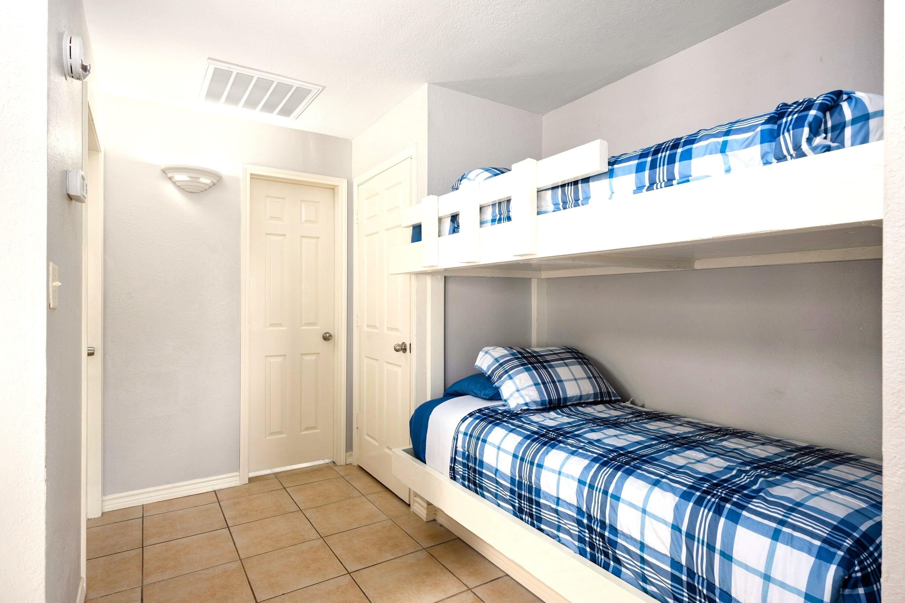 Une petite pièce avec un seul lit, un lit superposé, une porte et un luminaire fixé au mur.