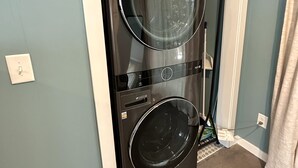 Una lavadora y secadora frontales negras de LG en una habitación con paredes color turquesa y un marco de puerta blanco.