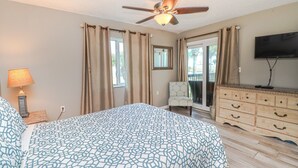 Ein Schlafzimmer mit Bett, Deckenventilator, Kommode, Stuhl und Fernseher.