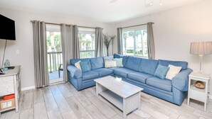Ein Wohnzimmer mit einem blauen Ecksofa, einem weißen Couchtisch und einem Fernseher auf einer Holzkommode.