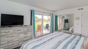 Ein Schlafzimmer mit einem Bett, einem Fernseher auf einer Kommode, einer Glasschiebetür zu einer Terrasse und einem Spiegel.