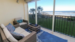 A balcony with wicker furniture, a blue rug, and a view of the ocean and beach.