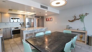 A modern kitchen with stainless steel appliances, a dining area with a large table and chairs, and a decorative sign on the wall.