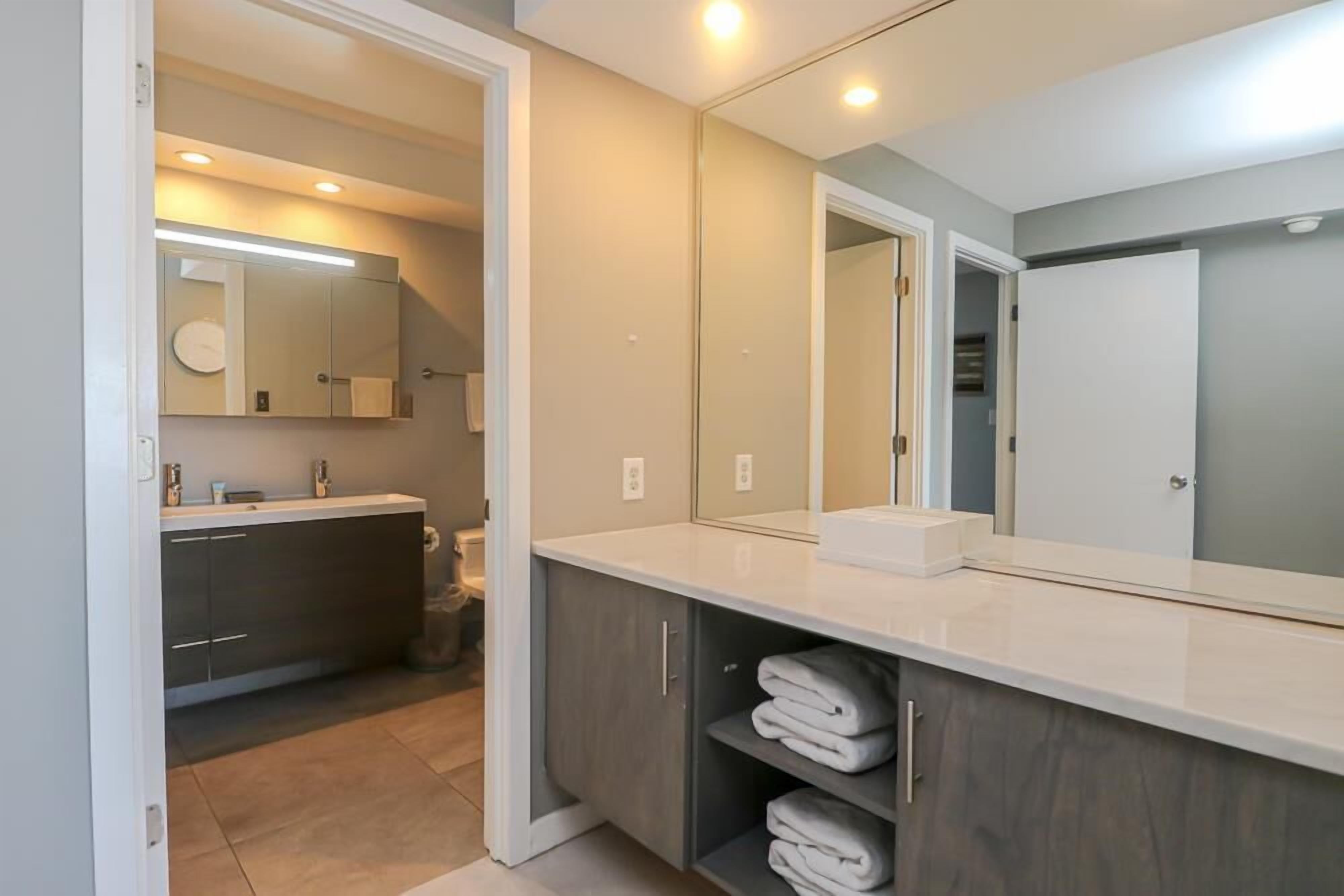 A modern bathroom with a large mirror, a sink, and a vanity with shelves for towels.