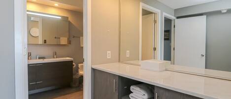 A modern bathroom with a large mirror, a sink, and a vanity with shelves for towels.
