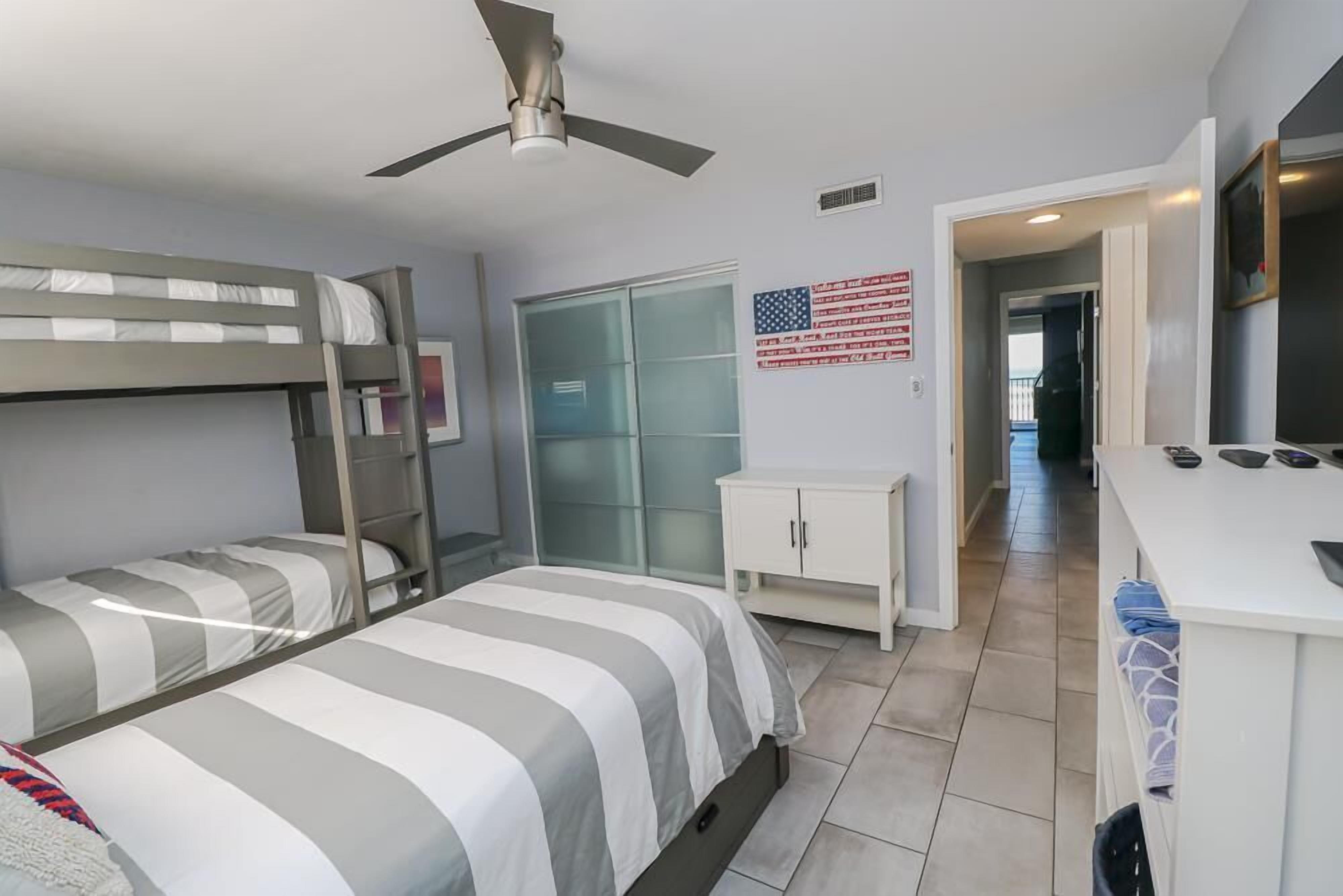 A bedroom with bunk beds, a desk, a television, and an American flag on the wall.