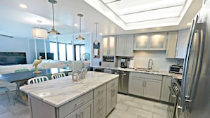 A modern kitchen with a large island, stainless steel appliances, and a dining area with a sofa and chairs.