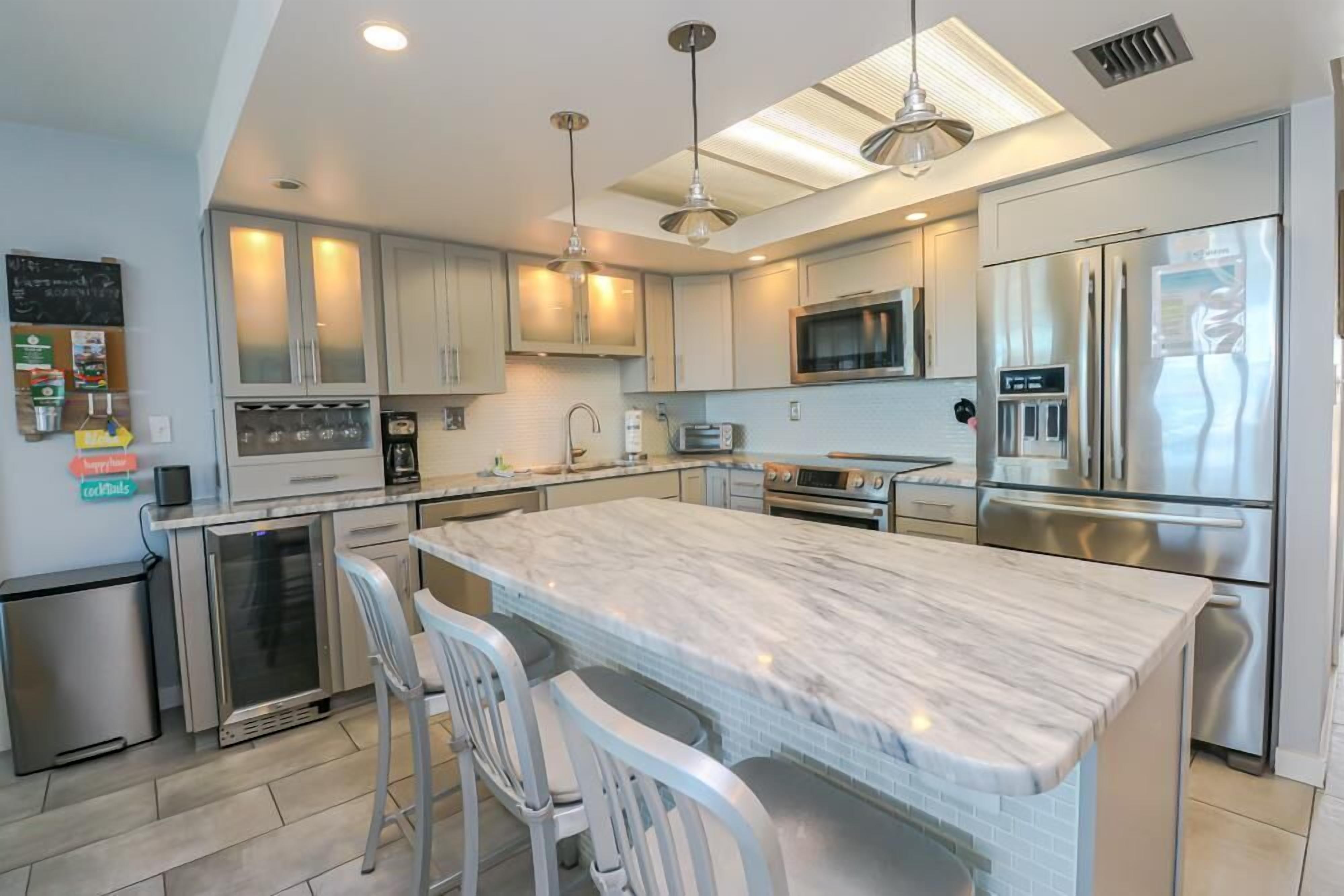 A modern kitchen with a marble island, stainless steel appliances, and pendant lighting.