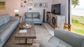 Een woonkamer met een bank, een salontafel, een televisie en uitzicht op het strand.